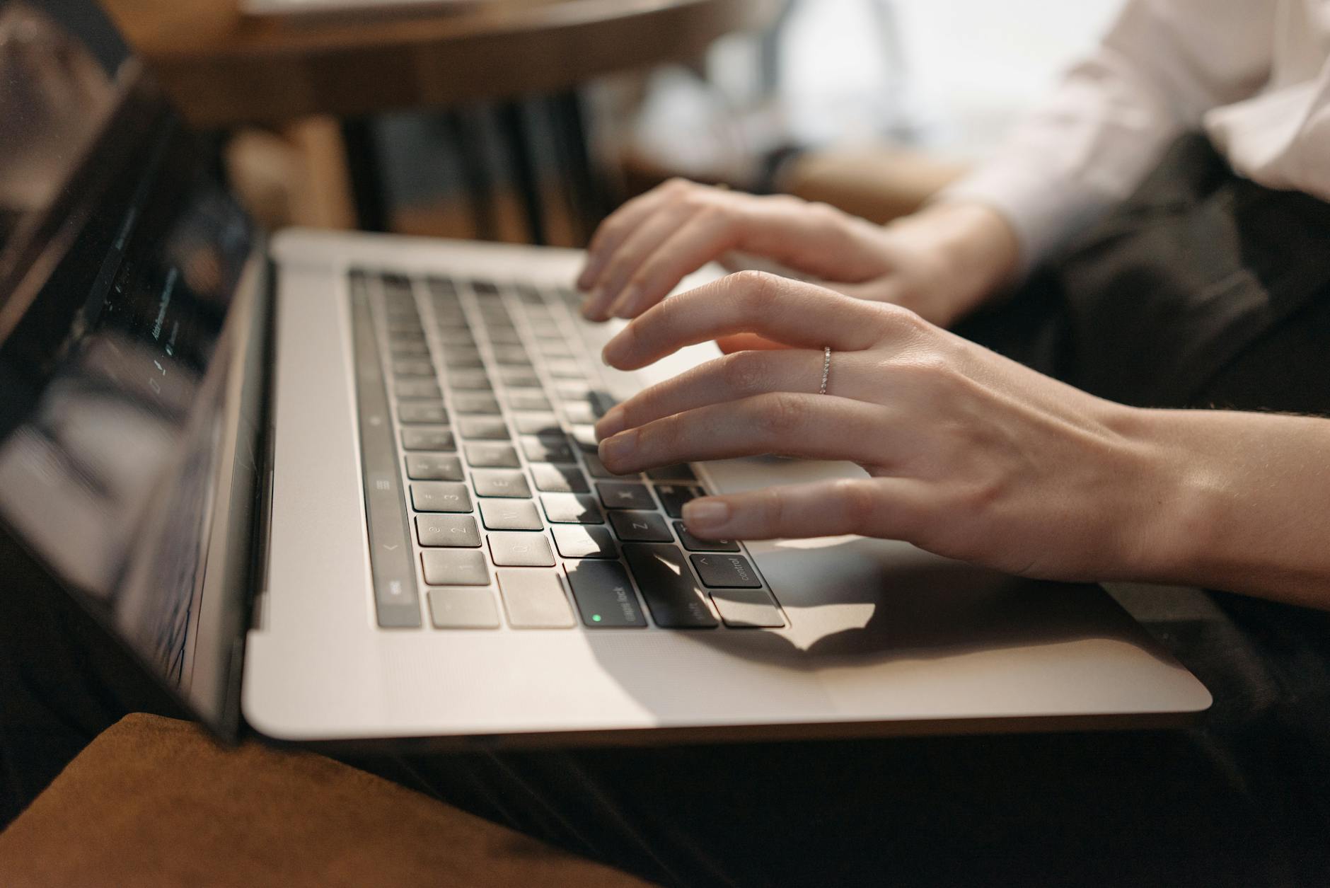 Close-up of hands typing on minimal keyboard with browser window reflecting clean typography and website grid layout on screen, soft warm side lighting, editorial product photography style